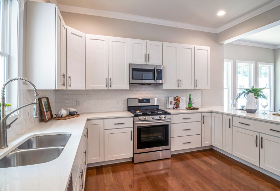 Bright remodeled kitchen with white cabinets, quartz countertops, stainless steel appliances, subway tile backsplash, large windows, and hardwood flooring.